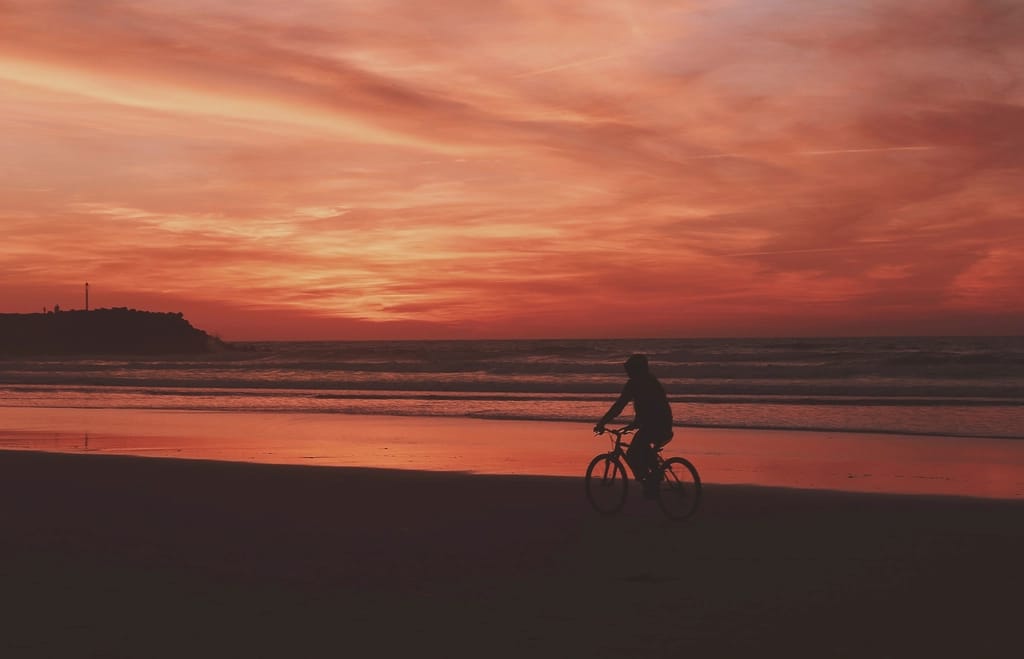 A cyclist silhouetted on the beach at sunset